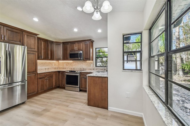 kitchen with lofted ceiling, appliances with stainless steel finishes, hanging light fixtures, tasteful backsplash, and light stone countertops