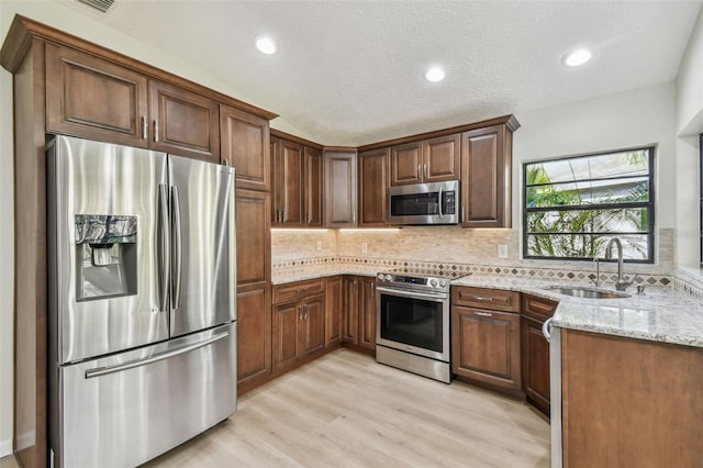 kitchen featuring sink, decorative backsplash, light hardwood / wood-style floors, light stone counters, and stainless steel appliances