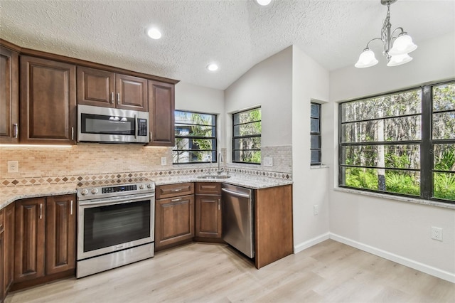 kitchen with sink, appliances with stainless steel finishes, light stone countertops, light hardwood / wood-style floors, and decorative backsplash