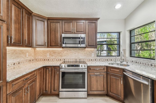 kitchen with sink, stainless steel appliances, light stone counters, tasteful backsplash, and a textured ceiling