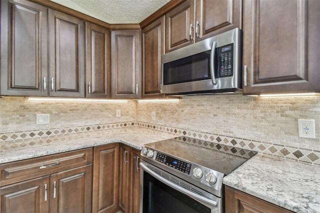 kitchen with backsplash, light stone countertops, a textured ceiling, and appliances with stainless steel finishes