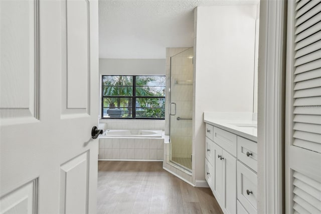 bathroom featuring plus walk in shower, hardwood / wood-style floors, vanity, and a textured ceiling