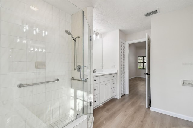 bathroom featuring an enclosed shower, vanity, wood-type flooring, and a textured ceiling