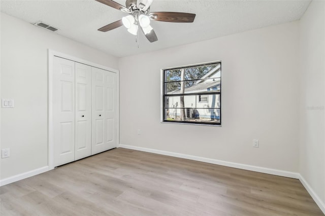 unfurnished bedroom featuring ceiling fan, a textured ceiling, a closet, and light wood-type flooring