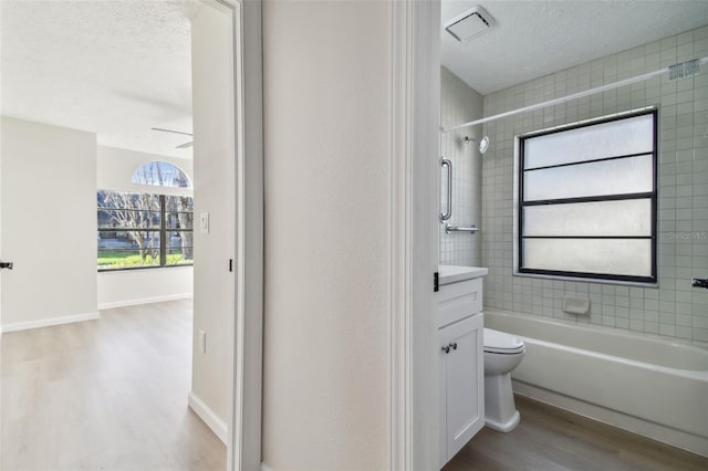 full bathroom with toilet, wood-type flooring, a textured ceiling, vanity, and tiled shower / bath combo