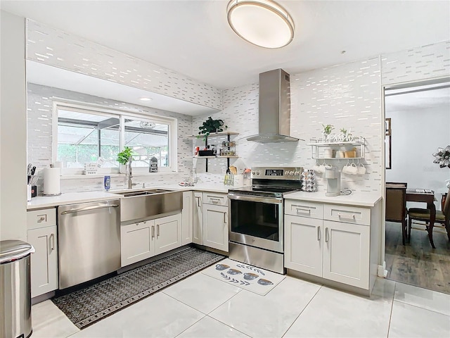 kitchen with wall chimney range hood, sink, appliances with stainless steel finishes, light tile patterned flooring, and decorative backsplash