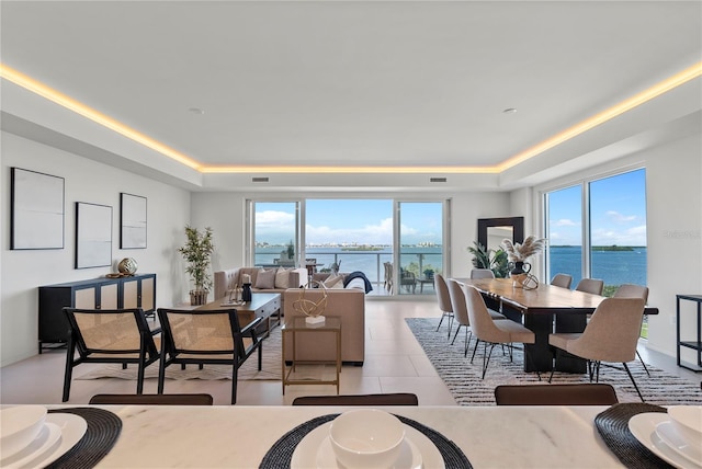 tiled dining room featuring a raised ceiling, a healthy amount of sunlight, and a water view