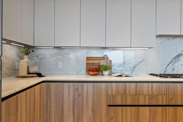 kitchen featuring decorative backsplash, stainless steel gas cooktop, and white cabinets