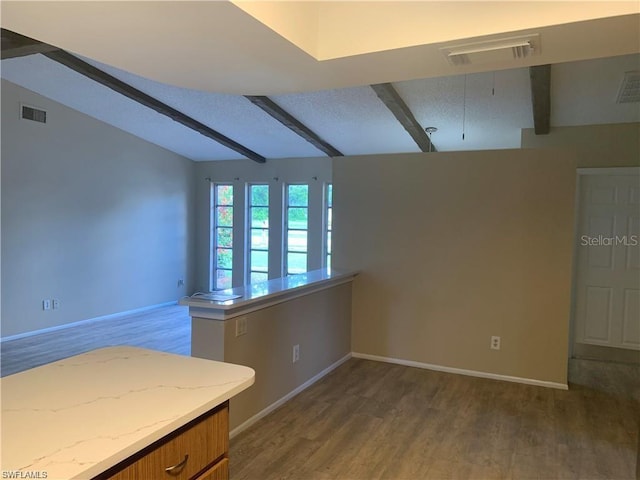 unfurnished room featuring hardwood / wood-style flooring, a textured ceiling, and vaulted ceiling with beams