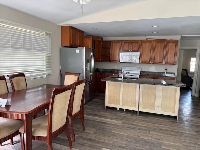 kitchen with lofted ceiling, white appliances, dark stone countertops, a center island with sink, and dark hardwood / wood-style flooring