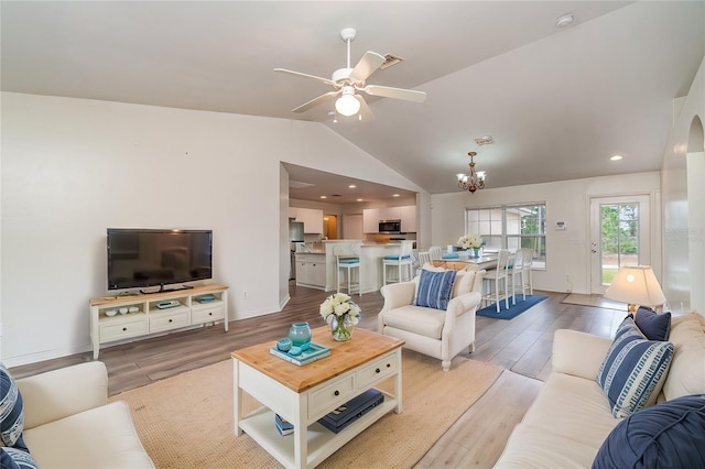 living room with ceiling fan with notable chandelier, vaulted ceiling, and light wood-type flooring