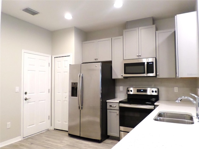 kitchen featuring stainless steel appliances, sink, white cabinets, and light hardwood / wood-style flooring