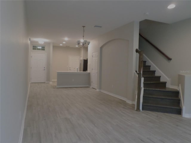 unfurnished living room with an inviting chandelier and light wood-type flooring