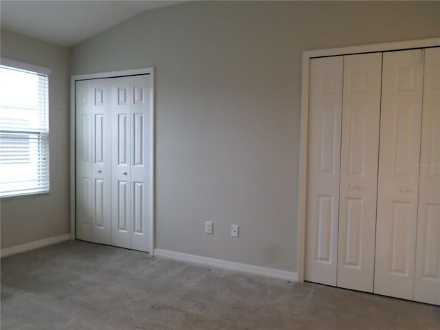 unfurnished bedroom featuring vaulted ceiling, two closets, and light colored carpet