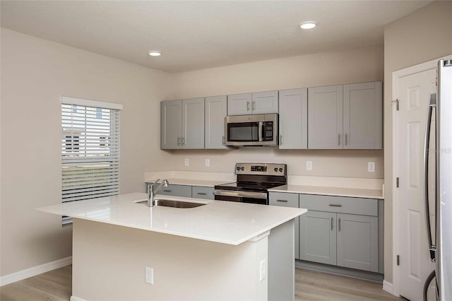 kitchen with an island with sink, appliances with stainless steel finishes, gray cabinets, and sink