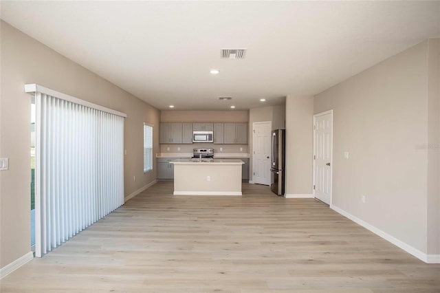 kitchen with gray cabinets, an island with sink, appliances with stainless steel finishes, and light hardwood / wood-style flooring