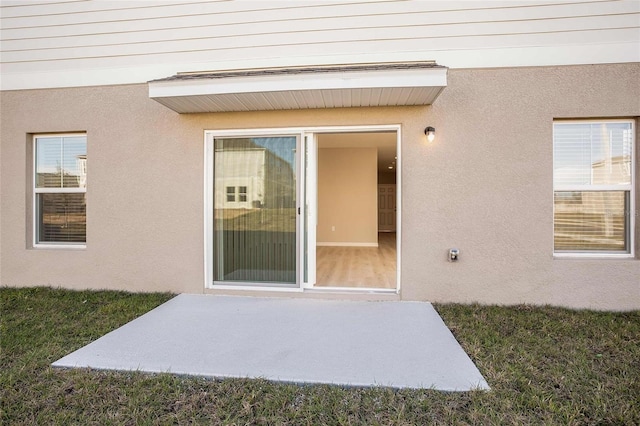 view of exterior entry with a patio and a lawn