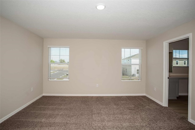 unfurnished room featuring a healthy amount of sunlight, dark carpet, and a textured ceiling