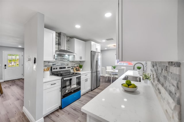 kitchen featuring sink, wall chimney range hood, stainless steel appliances, light stone countertops, and white cabinets