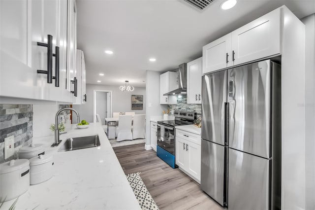 kitchen with sink, light stone counters, white cabinets, stainless steel appliances, and wall chimney range hood