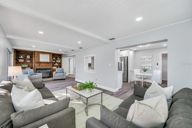 living room with beam ceiling, a fireplace, and light wood-type flooring