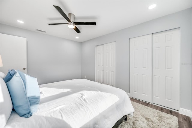 bedroom with two closets, dark hardwood / wood-style floors, and ceiling fan