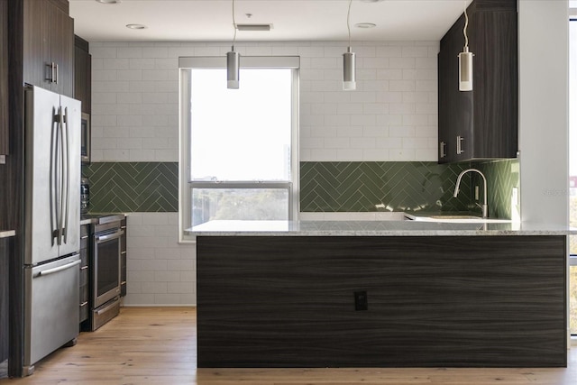 kitchen with appliances with stainless steel finishes, hanging light fixtures, kitchen peninsula, light stone countertops, and dark brown cabinets