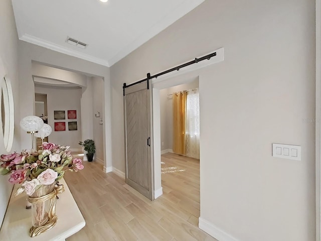 corridor featuring ornamental molding, a barn door, and light wood-type flooring