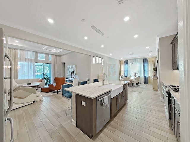 kitchen featuring crown molding, appliances with stainless steel finishes, sink, and a center island with sink