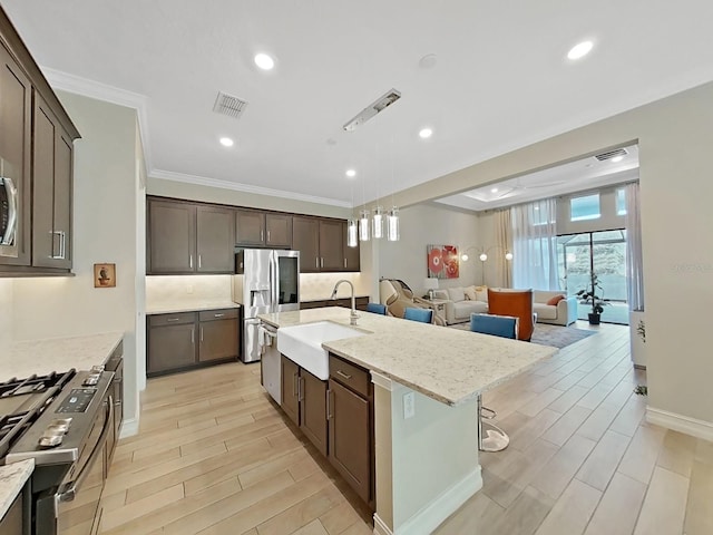 kitchen featuring appliances with stainless steel finishes, sink, light stone counters, dark brown cabinetry, and a center island with sink