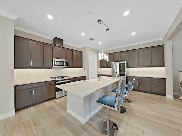 kitchen featuring sink, appliances with stainless steel finishes, dark brown cabinets, a center island with sink, and decorative light fixtures