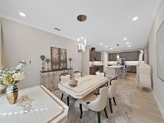 dining area with an inviting chandelier, crown molding, and light hardwood / wood-style floors