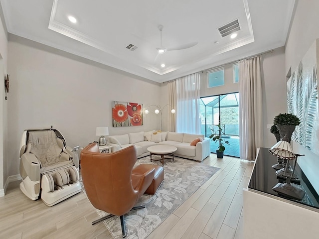 living room featuring ceiling fan, ornamental molding, and a raised ceiling