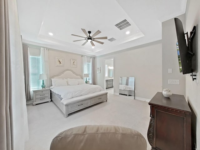 carpeted bedroom with ceiling fan, ensuite bathroom, a raised ceiling, and multiple windows