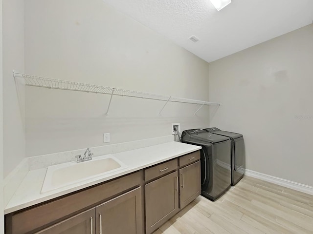 laundry area featuring sink, cabinets, a textured ceiling, washer and dryer, and light hardwood / wood-style flooring