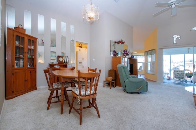 dining area with light carpet, ceiling fan with notable chandelier, and a high ceiling