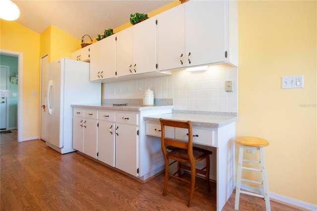 kitchen featuring white cabinetry, wood-type flooring, a kitchen breakfast bar, white fridge, and backsplash