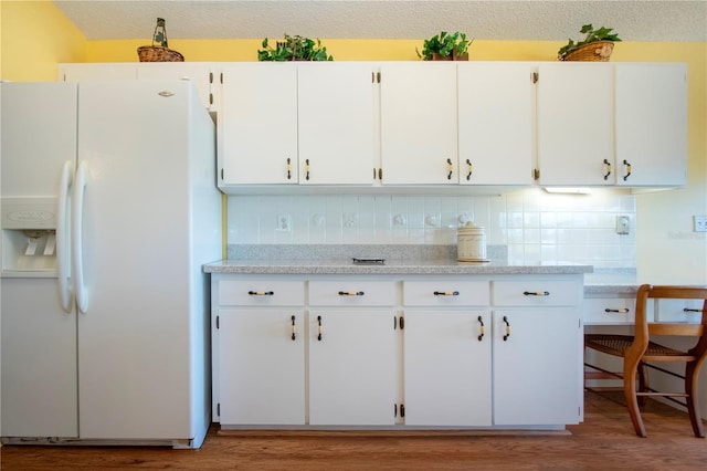 kitchen featuring a textured ceiling, backsplash, white fridge with ice dispenser, hardwood / wood-style flooring, and white cabinets