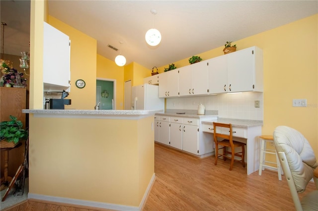 kitchen with hanging light fixtures, white fridge with ice dispenser, white cabinets, and kitchen peninsula