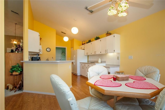 dining area with ceiling fan with notable chandelier, vaulted ceiling, and light wood-type flooring