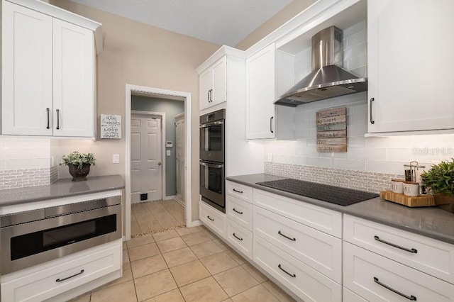 kitchen with white cabinets, black appliances, decorative backsplash, and wall chimney range hood