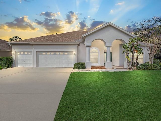 ranch-style home featuring concrete driveway, roof with shingles, a front yard, stucco siding, and a garage