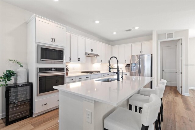 kitchen with stainless steel appliances, white cabinetry, sink, and beverage cooler