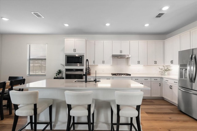 kitchen with sink, white cabinetry, light hardwood / wood-style flooring, appliances with stainless steel finishes, and a kitchen island with sink