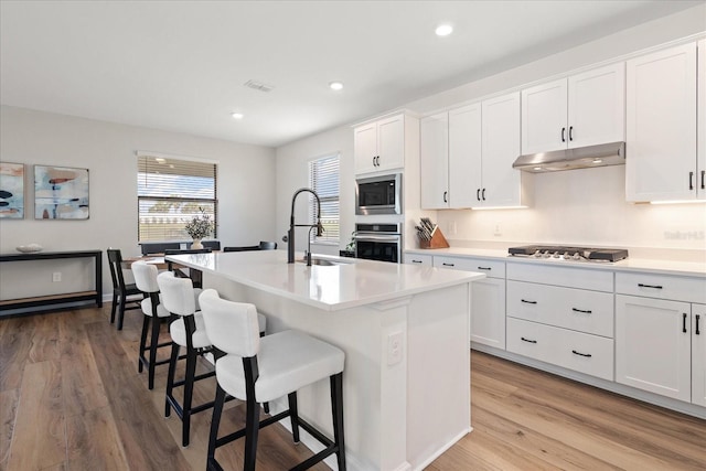 kitchen featuring sink, white cabinets, a kitchen breakfast bar, stainless steel appliances, and a center island with sink