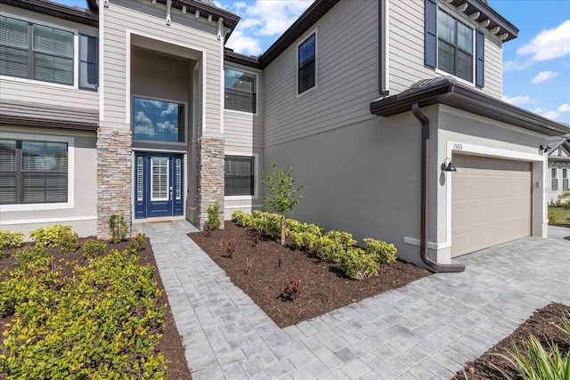 view of front of home with driveway, stone siding, a garage, and stucco siding