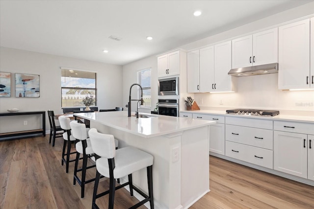 kitchen featuring a sink, light wood-style floors, under cabinet range hood, a kitchen bar, and stainless steel appliances