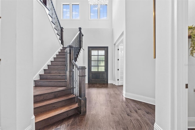 foyer entrance with a notable chandelier, a towering ceiling, and dark hardwood / wood-style floors