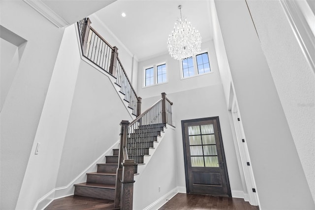 entryway with a towering ceiling, ornamental molding, dark hardwood / wood-style floors, and a notable chandelier