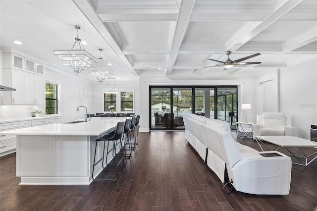 kitchen with sink, a breakfast bar area, white cabinetry, hanging light fixtures, and a center island with sink